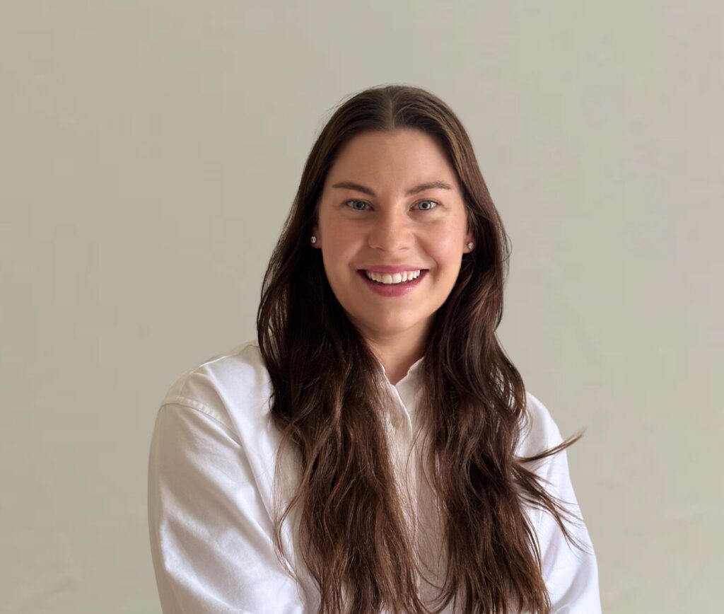 Jess Stolberg with long hair smiling in a white shirt